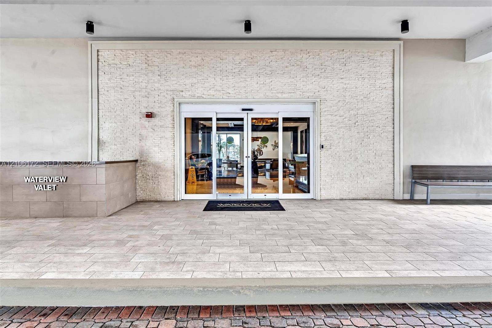 20515 E Country Club Drive, #246, Aventura, Aventura, FL 33180 Covered valet entrance featuring a textured stone facade, automated glass sliding doors, recessed ceiling lighting, and paved stone flooring