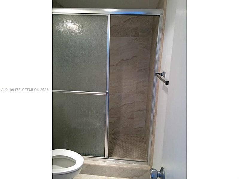 20515 E Country Club Drive, #246, Aventura, Aventura, FL 33180 Walk-in shower featuring a sliding glass door, full-height stone-finish wall tile, mosaic tile shower floor, and metallic hardware