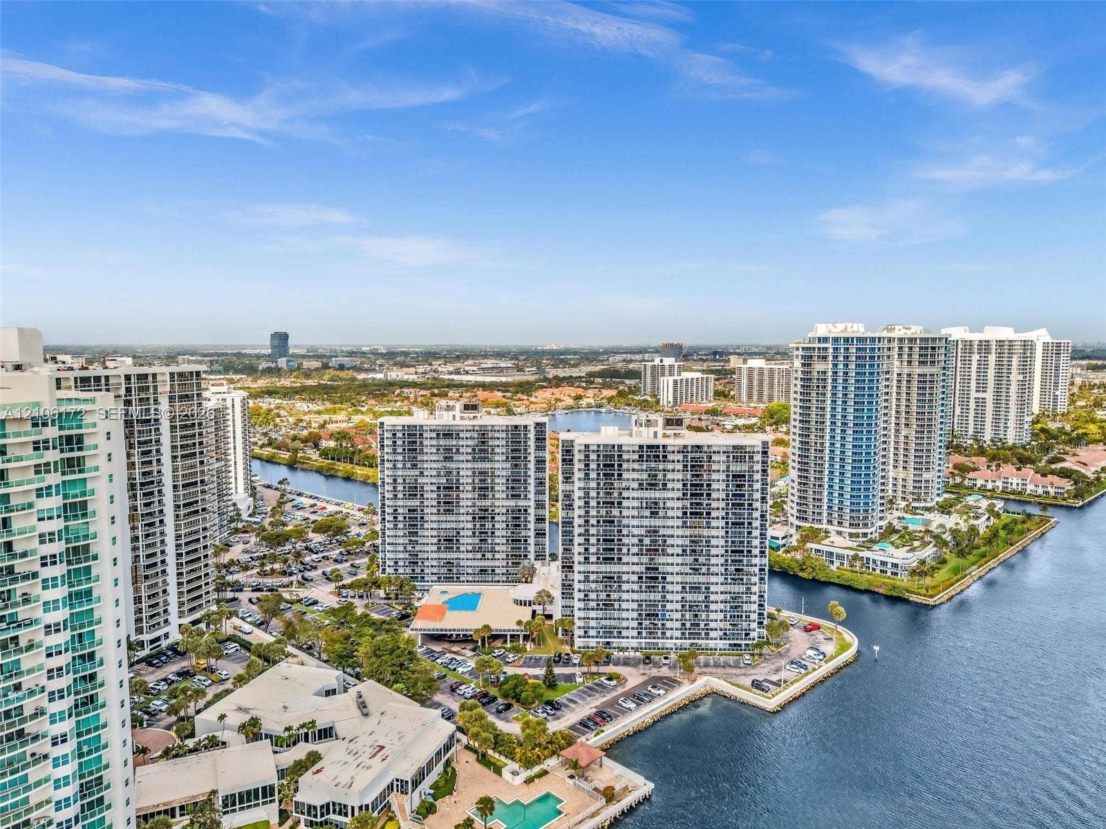 20515 E Country Club Drive, #246, Aventura, Aventura, FL 33180 Aerial perspective of high-rise residential buildings situated along a waterway, featuring manicured landscaping, paved parking areas, and ground-level swimming pools