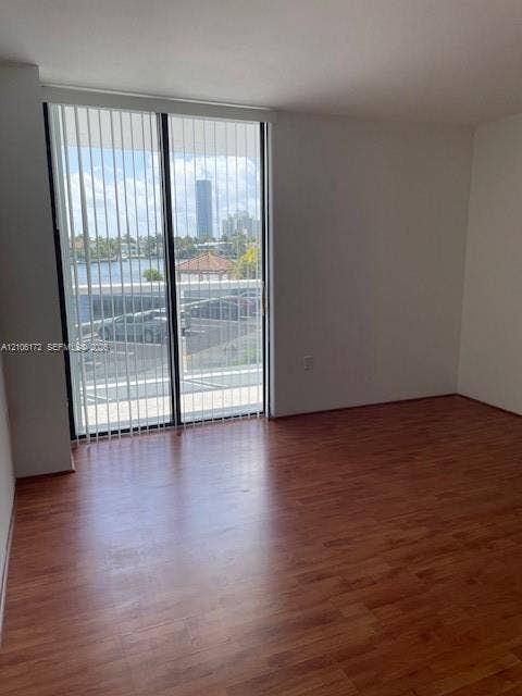 20515 E Country Club Drive, #246, Aventura, Aventura, FL 33180 Wood-finish flooring and floor-to-ceiling sliding glass doors with vertical blinds, providing natural light and exterior water scenery