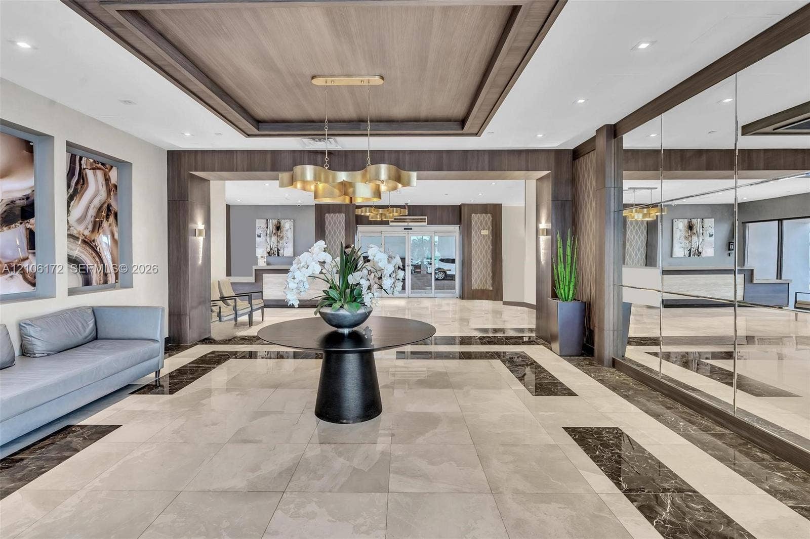 20515 E Country Club Drive, #246, Aventura, Aventura, FL 33180 Grand lobby featuring tile flooring with dark stone inlay, coffered wood-paneled ceiling, large-scale gold-finish chandelier, and full-height mirrored wall panels