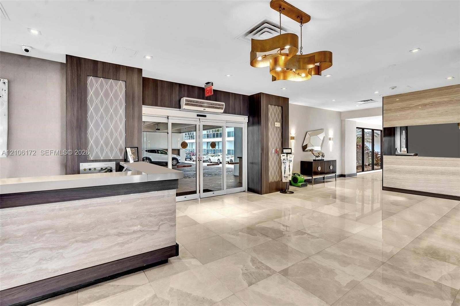 20515 E Country Club Drive, #246, Aventura, Aventura, FL 33180 Lobby area featuring polished tile flooring, a custom reception desk with stone-finish surfaces and dark wood-tone cabinetry, a sculptural gold-tone pendant light fixture, and floor-to-ceiling glass entry doors