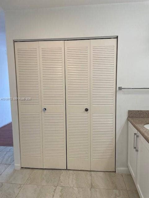 20515 E Country Club Drive, #246, Aventura, Aventura, FL 33180 Bi-fold closet doors featuring white louvered panels, light-toned stone-finish tile flooring, and built-in vanity with a stone-finish countertop