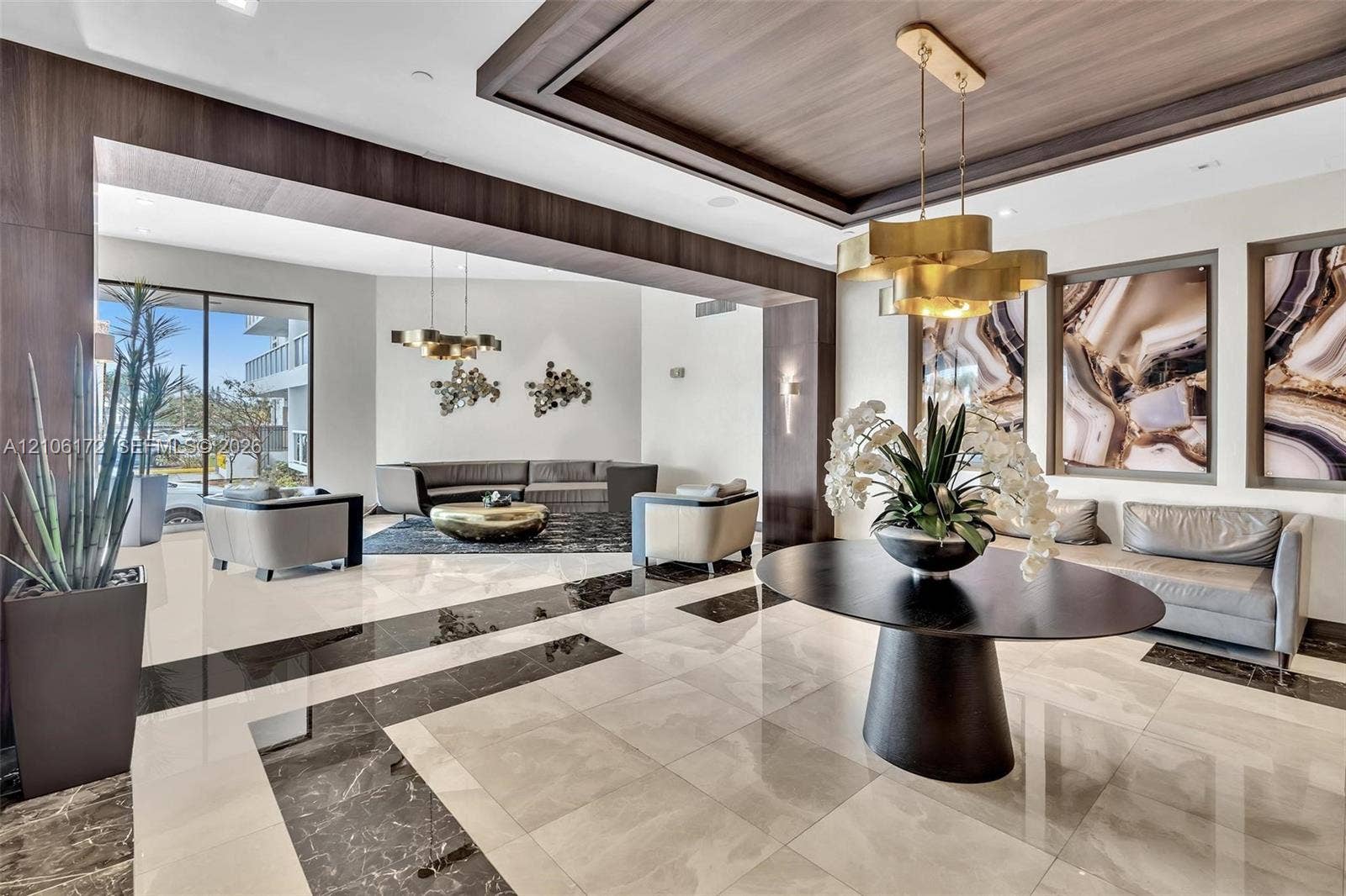 20515 E Country Club Drive, #246, Aventura, Aventura, FL 33180 Large-format polished tile flooring featuring high-contrast geometric stone inlay, recessed tray ceiling with wood-finish paneling, custom-designed metallic tiered chandeliers, and extensive wood-finish wall paneling