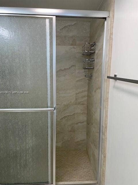 20515 E Country Club Drive, #246, Aventura, Aventura, FL 33180 Shower enclosure featuring a sliding glass door, floor-to-ceiling neutral-toned tile surround, mosaic tile flooring, and integrated metal shelving
