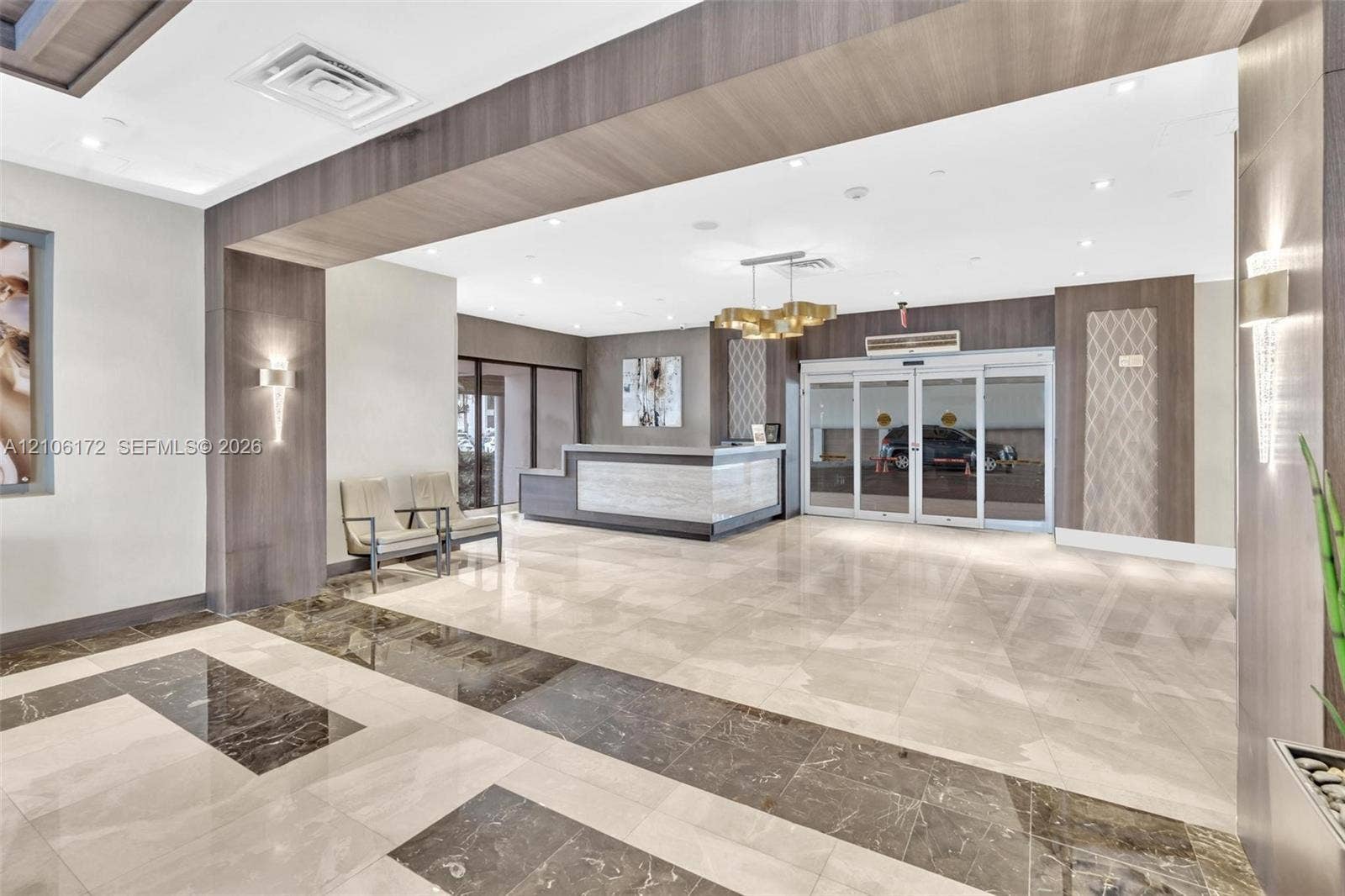 20515 E Country Club Drive, #246, Aventura, Aventura, FL 33180 Entrance lobby featuring polished stone flooring, custom stone reception desk, recessed ceiling lighting, wood-finish wall paneling, and glass sliding entry doors