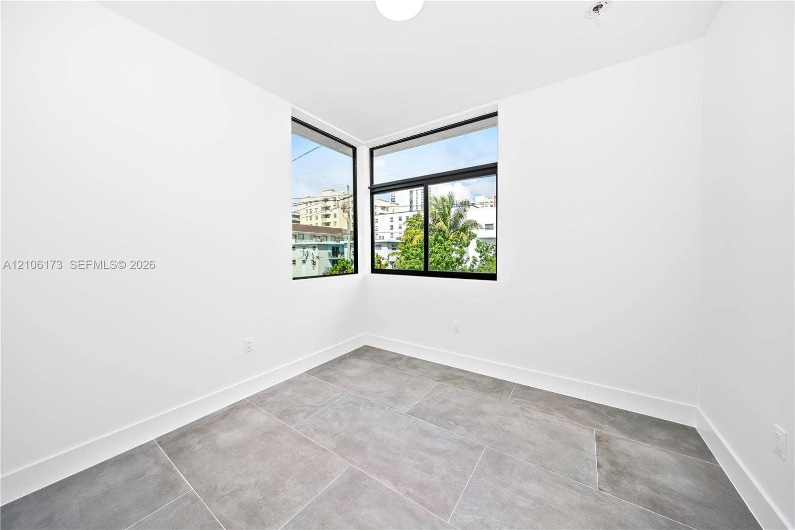 Corner room featuring large format stone-finish tile flooring, white walls, and black-framed windows