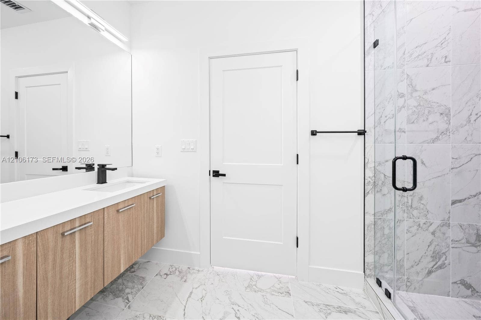 Floating wood-finish vanity with an integrated sink, polished stone-finish flooring, glass-enclosed shower with full-height tile surround, and matte black fixtures