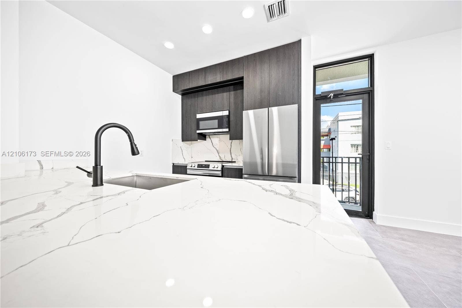 Kitchen featuring stone-patterned countertops, dark wood-finish cabinetry, stainless steel appliances, and a matte black pull-down faucet