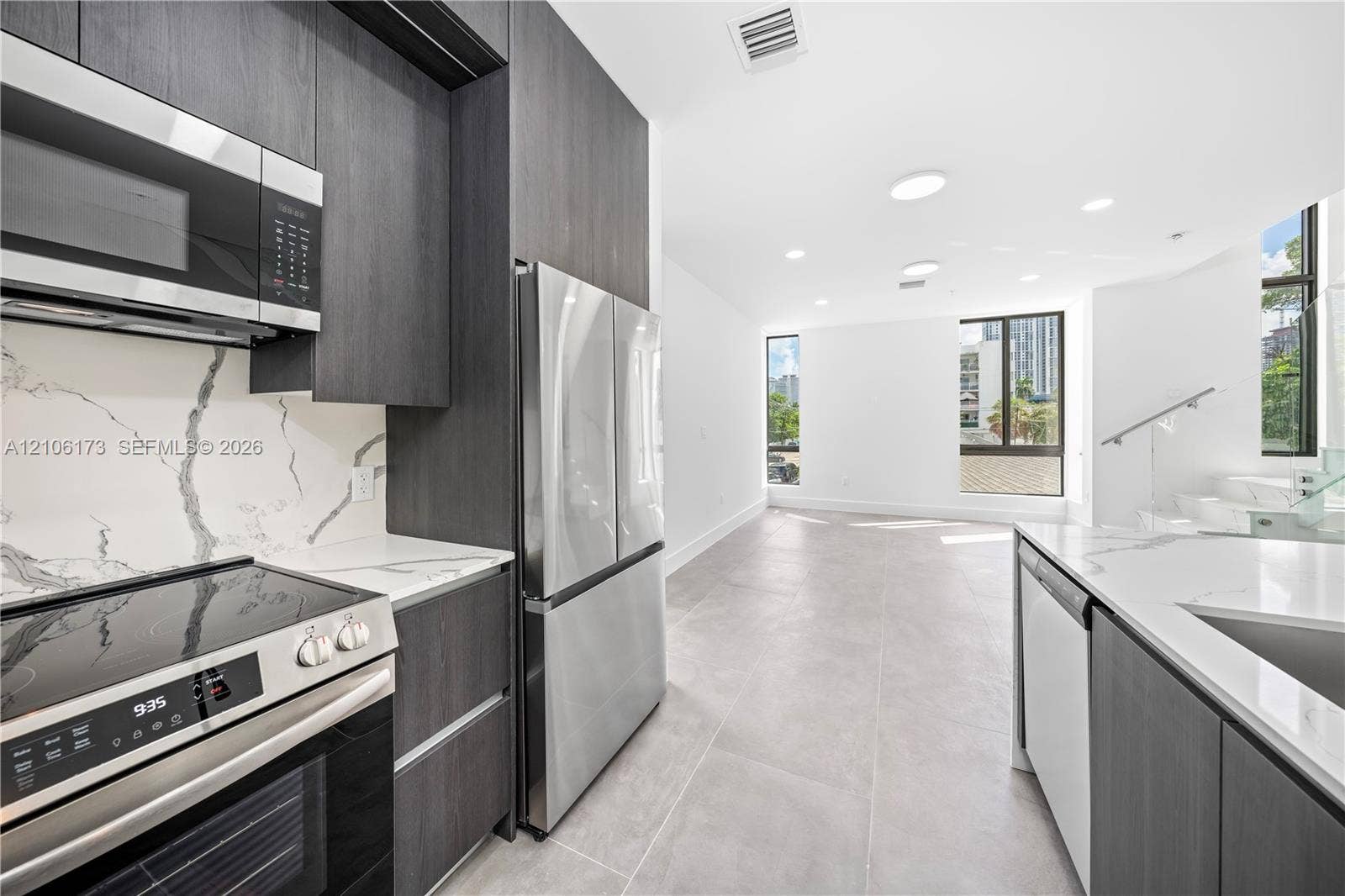 Kitchen featuring dark-finish cabinetry, stainless steel appliances, quartz countertops with full-height backsplashes, and large-format tile flooring