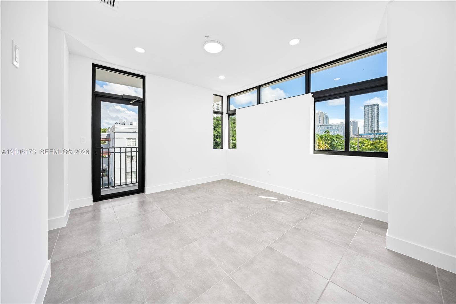 Room featuring large-format gray tile flooring, black-framed windows, clerestory windows, recessed lighting, and a glass-paneled door with an attached balcony
