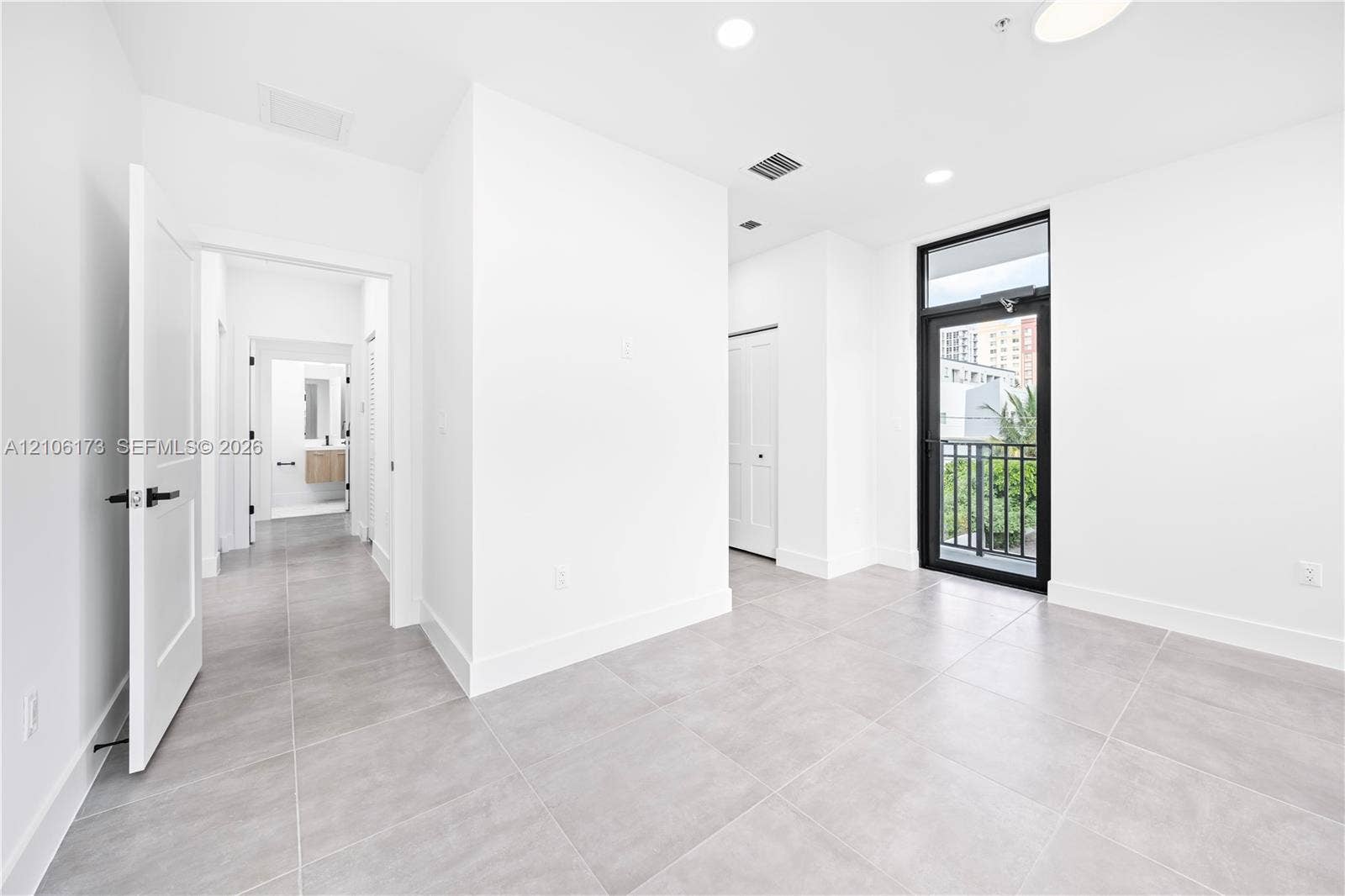 Neutral-toned tile flooring, recessed ceiling lighting, a door with a black frame and hardware, and a metal-railing balcony