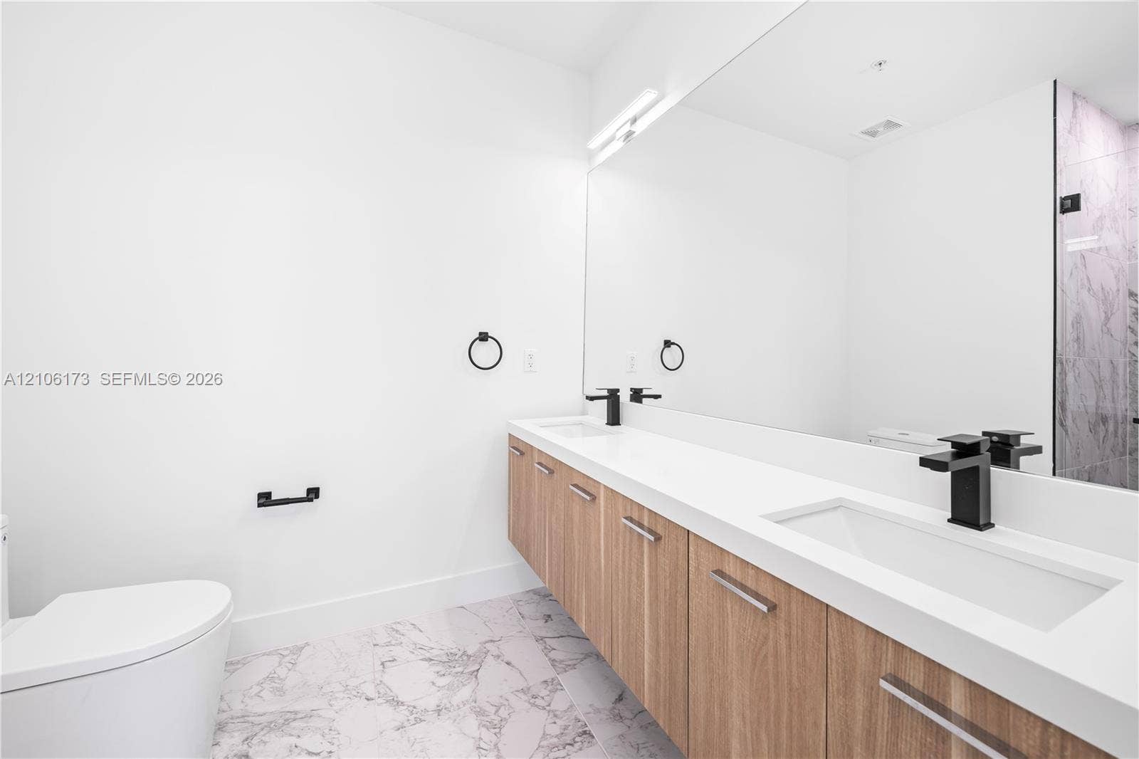 Floating wood-finish vanity with dual integrated rectangular sinks, white stone countertop, matte black faucets, and full-width wall mirror