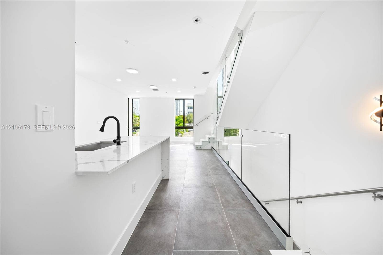 Kitchen featuring a waterfall-edge countertop, matte black faucet, integrated stainless steel sink, glass stair railing, and large-format tile flooring