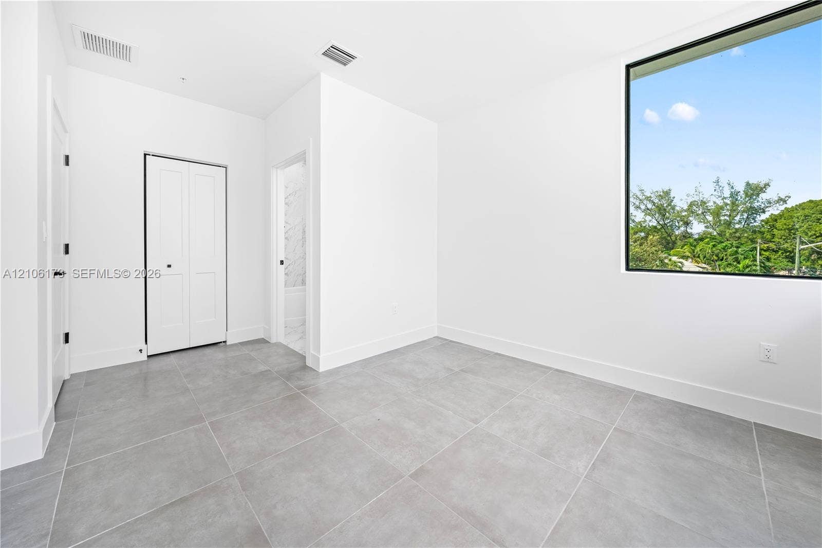 Interior space featuring large-format ceramic tile flooring, a floor-to-ceiling window with black trim, and a white bi-fold closet door