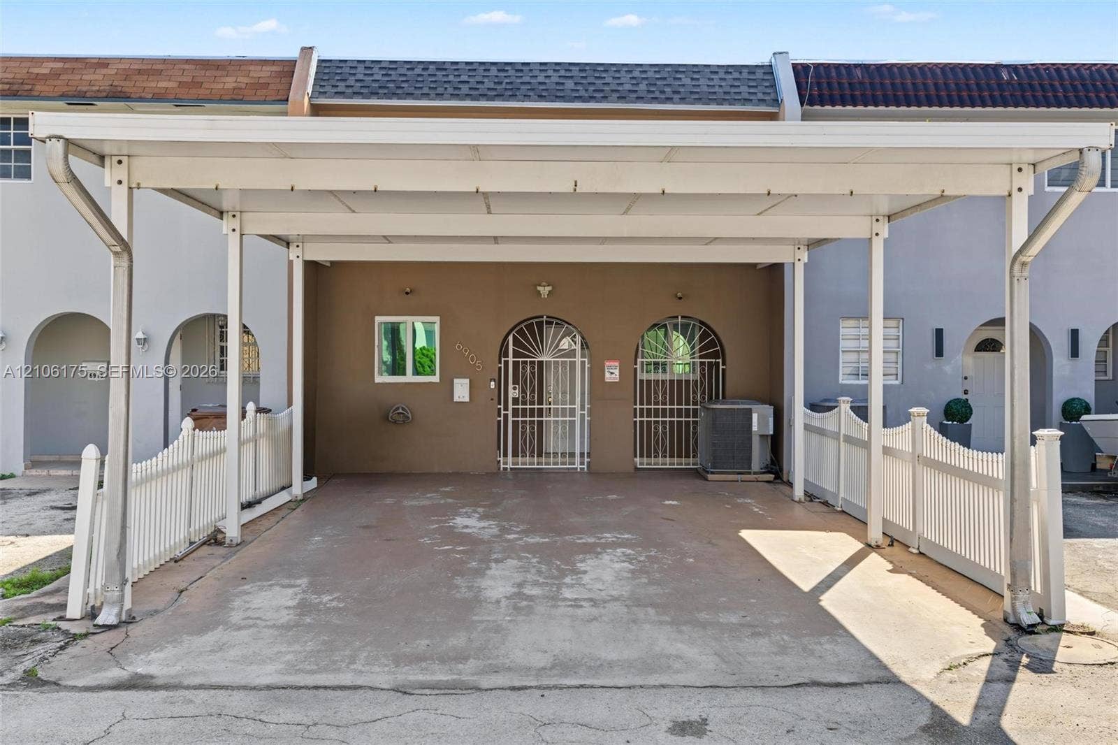 6905 W 2nd Way, #1, Hialeah, Hialeah, FL 33014 Covered carport featuring a concrete parking pad, white vinyl perimeter fencing, and dual arched metal security doors