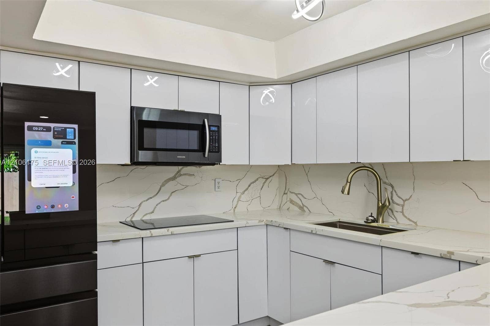 6905 W 2nd Way, #1, Hialeah, Hialeah, FL 33014 High-gloss white cabinetry featuring flat-panel doors, solid-surface countertops with integrated backsplash, built-in smart refrigerator, over-the-range microwave, and a gooseneck faucet