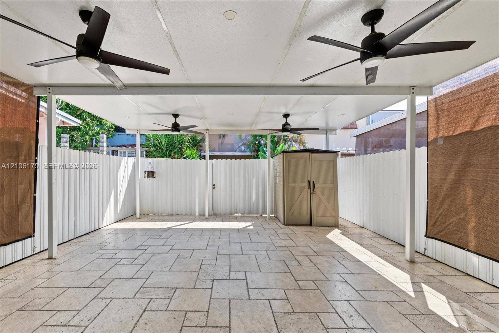 6905 W 2nd Way, #1, Hialeah, Hialeah, FL 33014 Covered patio featuring stone-tiled flooring, white metal privacy fencing, four ceiling-mounted fans, and an integrated storage unit