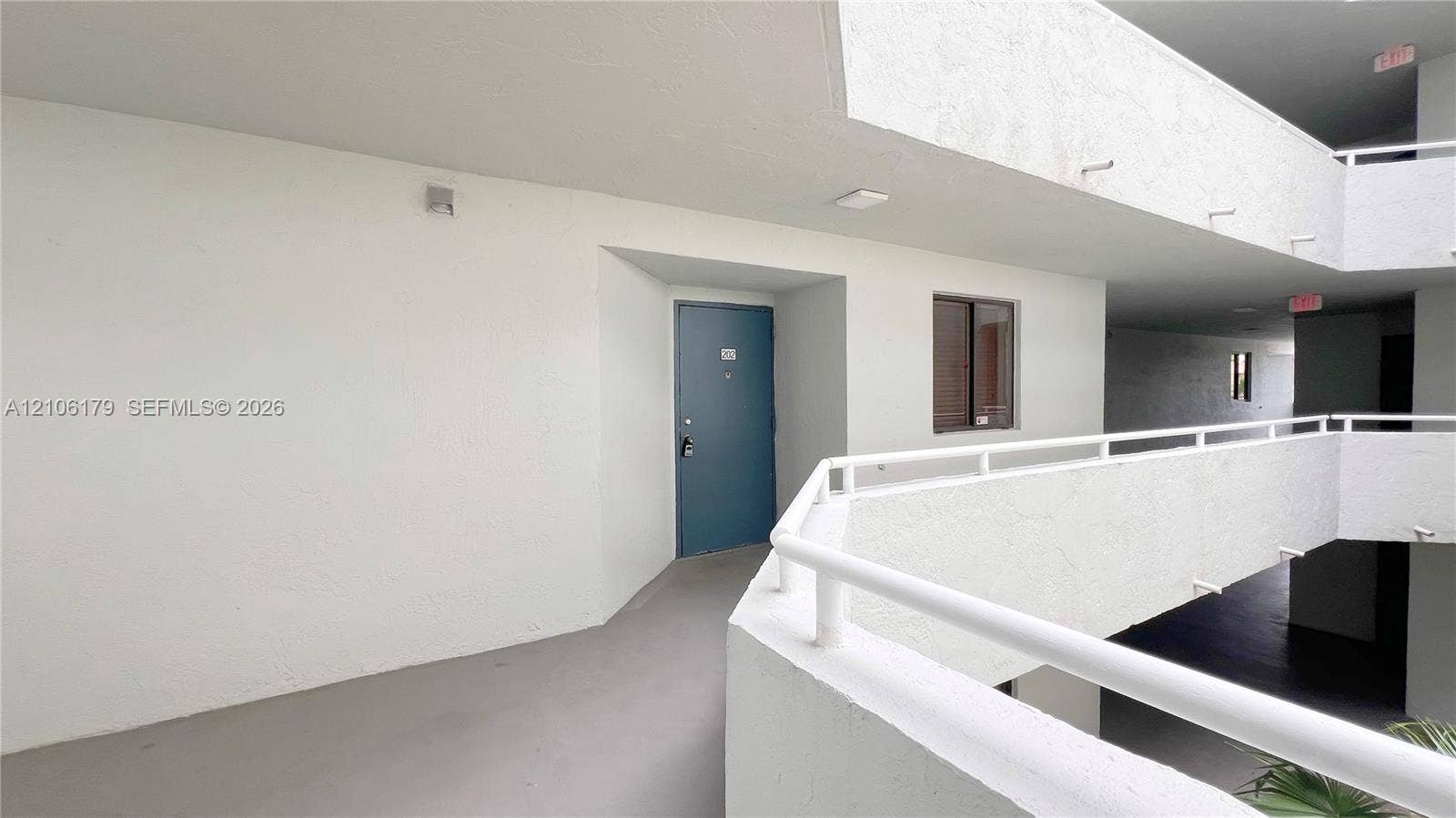 Open-air corridor featuring concrete flooring, stucco-textured walls, and white metal railings