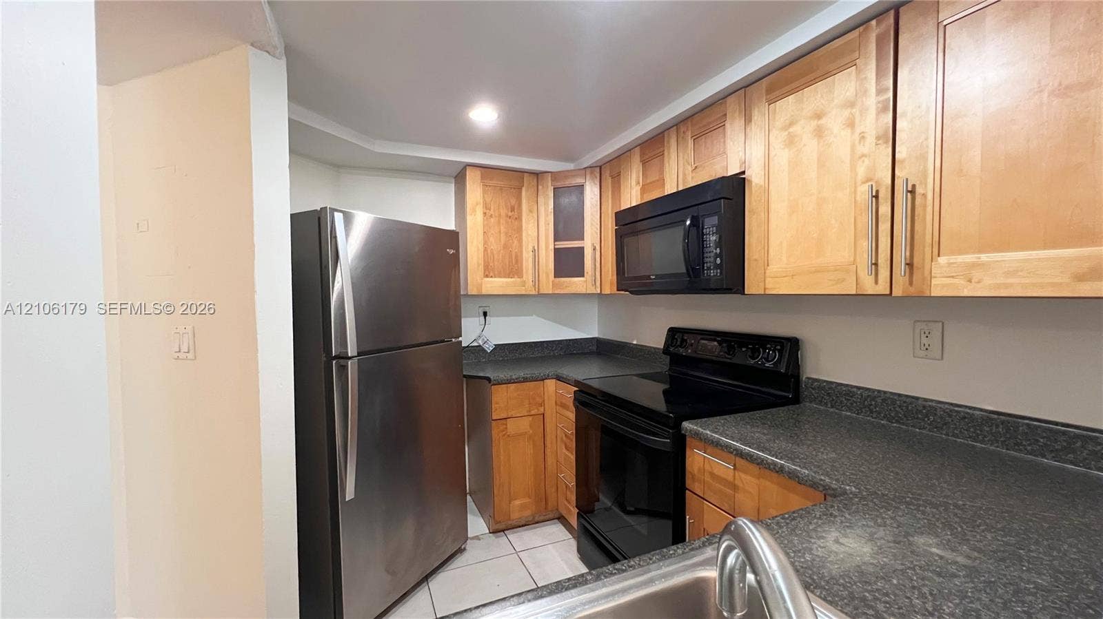 Kitchen featuring shaker-style wood cabinetry, dark stone-finish countertops, stainless steel refrigerator, black range, and black built-in microwave