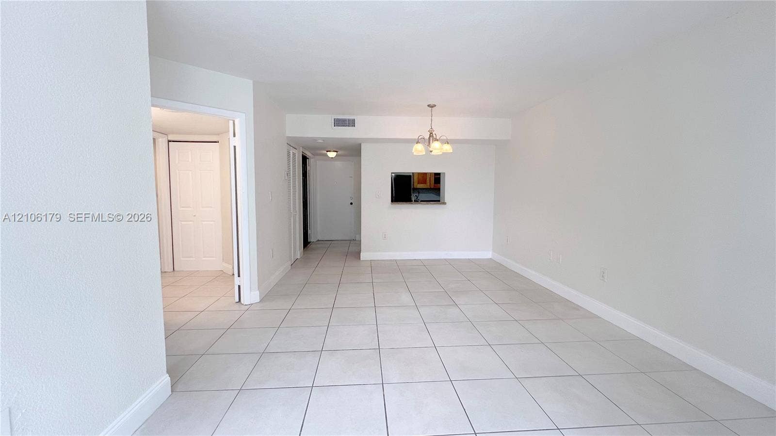 Neutral-toned ceramic tile flooring, multi-arm chandelier lighting, and kitchen pass-through window with interior ledge