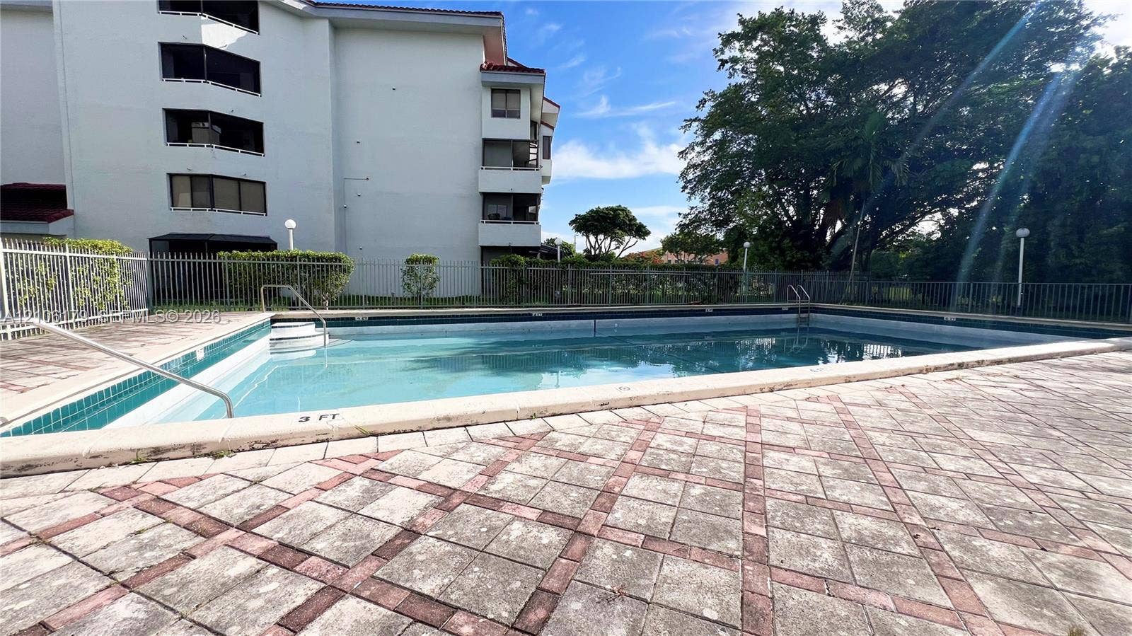 Outdoor swimming pool featuring a concrete deck with a patterned tile border and a metal safety fence enclosure