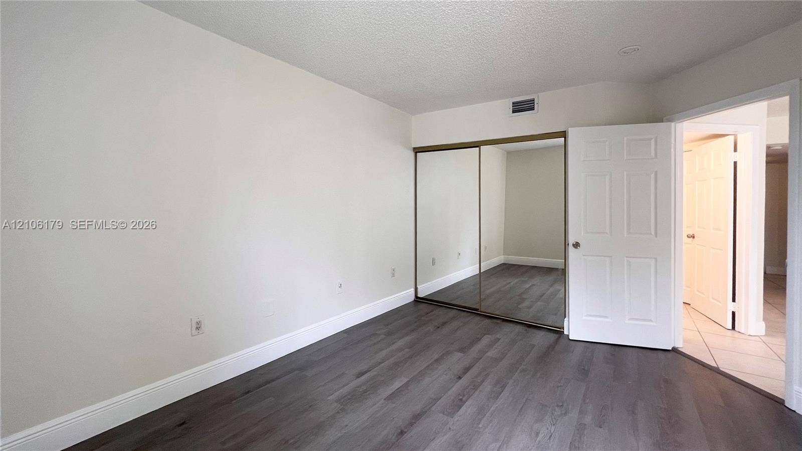 Room featuring wood-finish flooring, sliding mirror-panel closet doors, and six-panel interior door