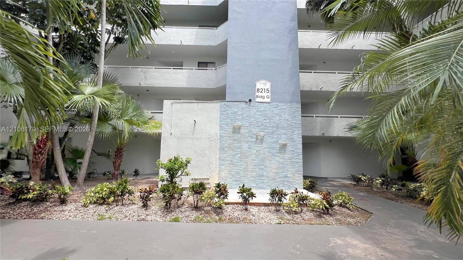 Multi-story building exterior featuring a stacked stone veneer facade, integrated water feature, recessed balconies, and mature palm landscaping