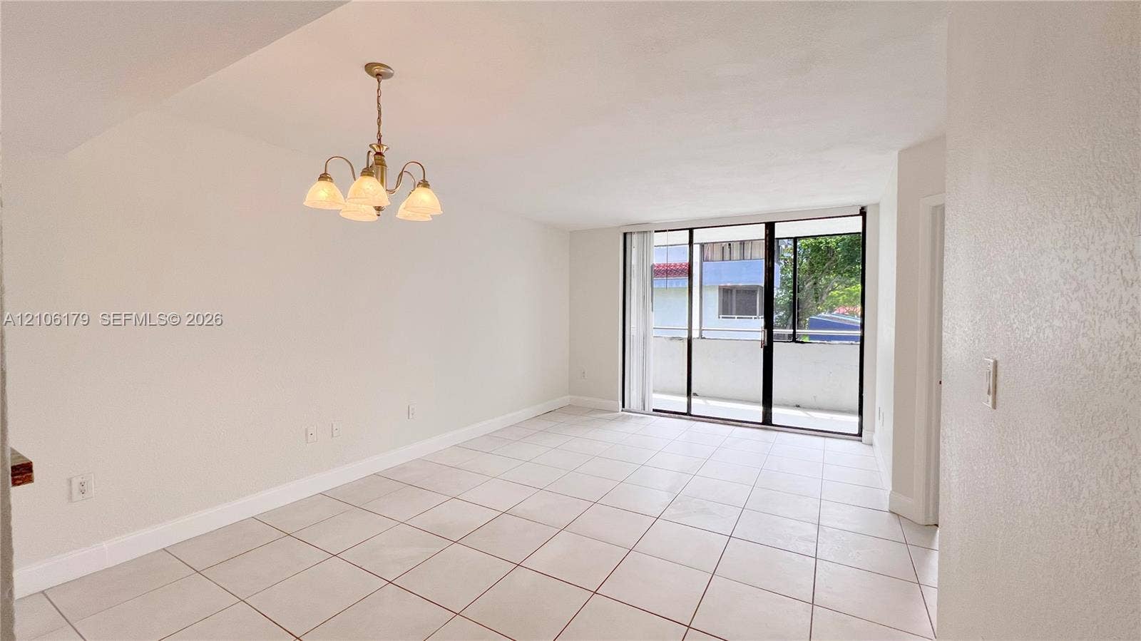 Bright interior space featuring light-colored floor tiling, a multi-arm chandelier, and floor-to-ceiling sliding glass doors leading to an exterior balcony