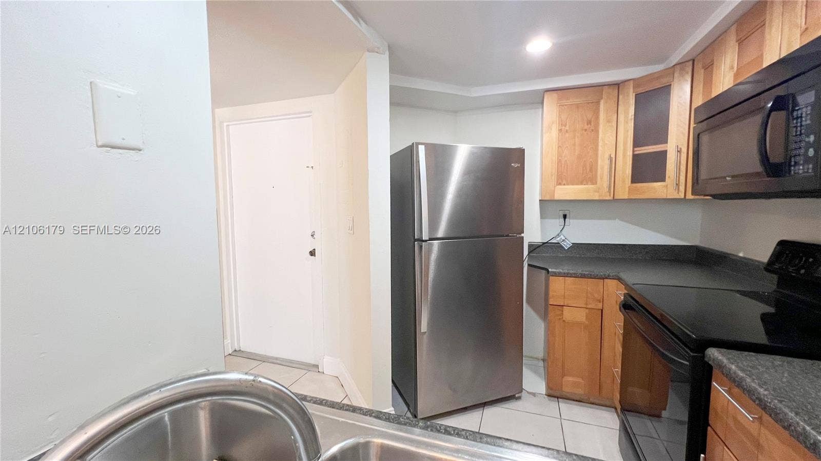 Kitchen featuring stainless steel refrigerator, dark solid-surface countertops, light wood-finish cabinetry, built-in microwave, and tile flooring