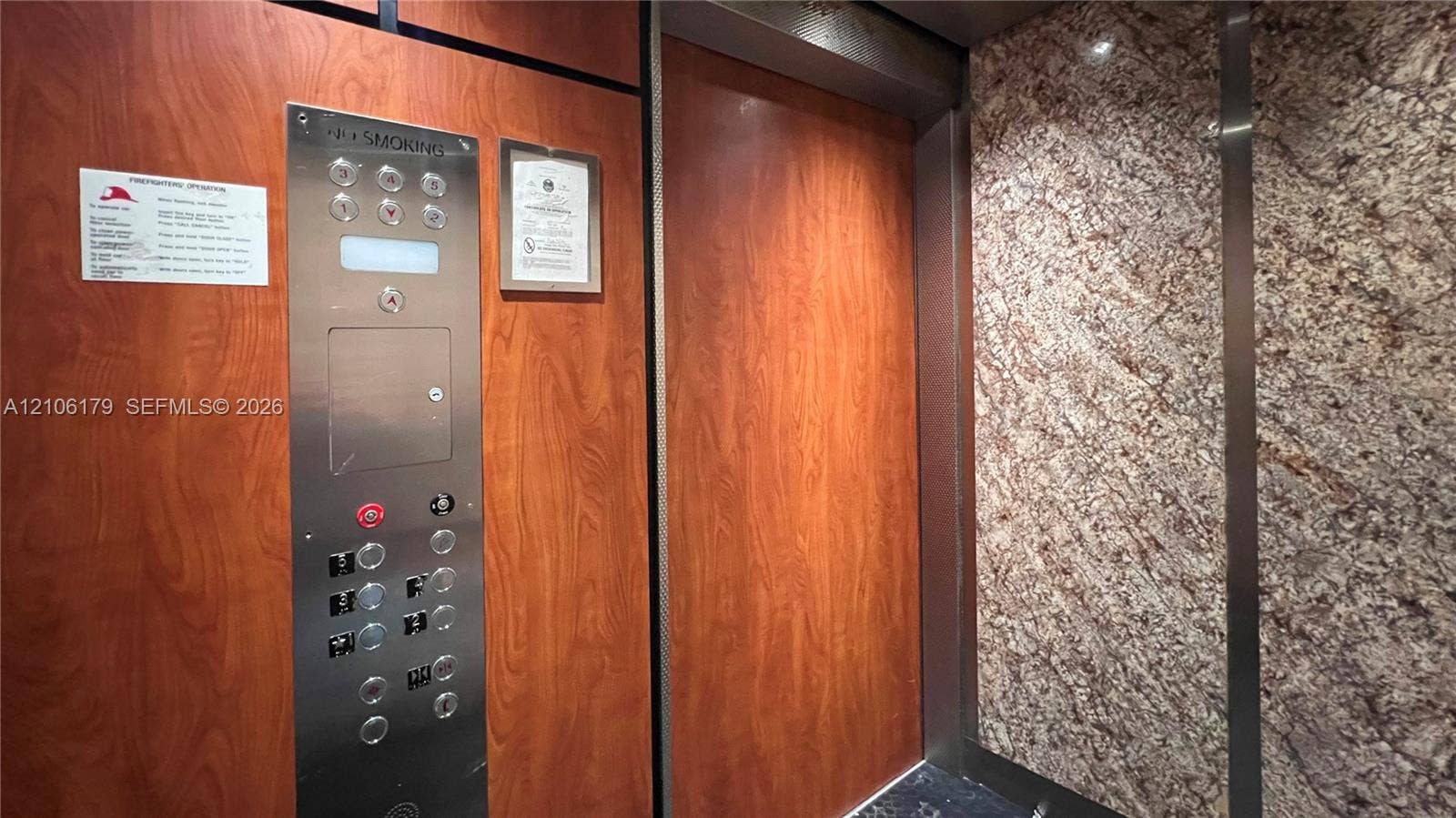 Elevator interior featuring wood-finish paneling, stone wall cladding, and a brushed stainless steel control panel