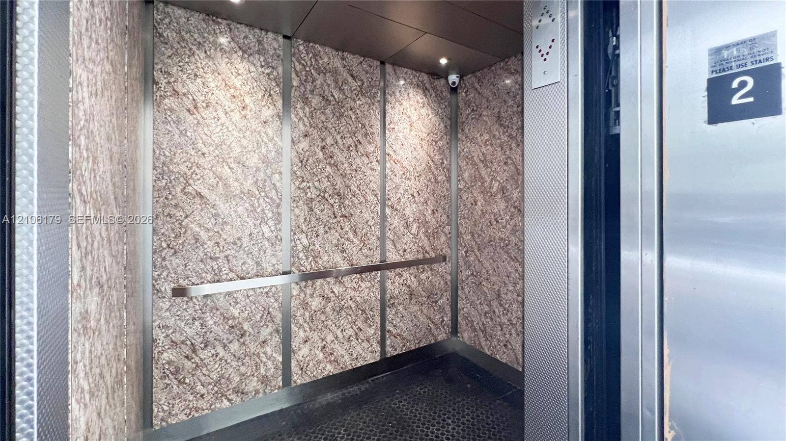 Elevator interior featuring patterned stone-finish wall panels, stainless steel trim, a horizontal grab bar, and recessed ceiling lighting