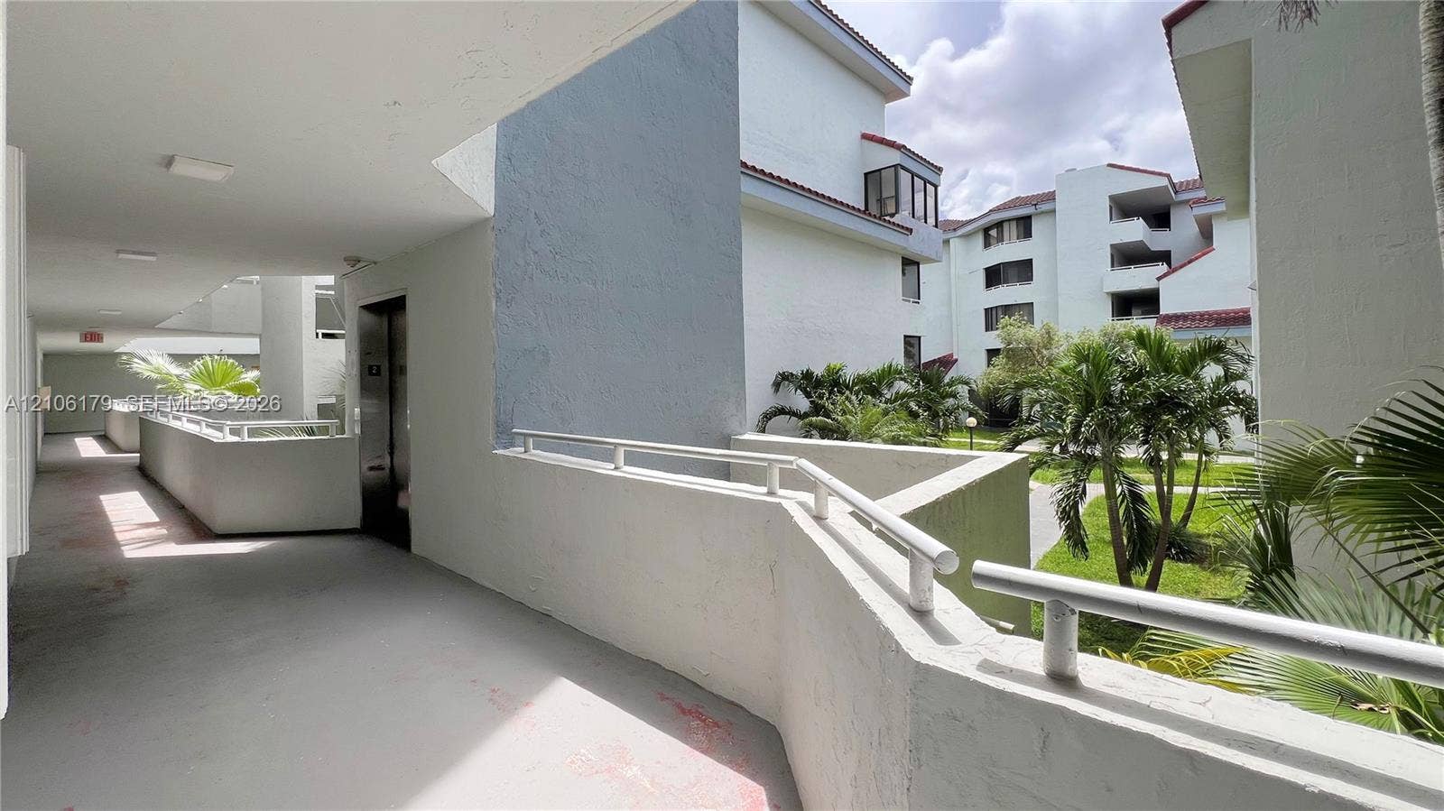 Covered exterior corridor featuring metal railing, concrete flooring, and building access points