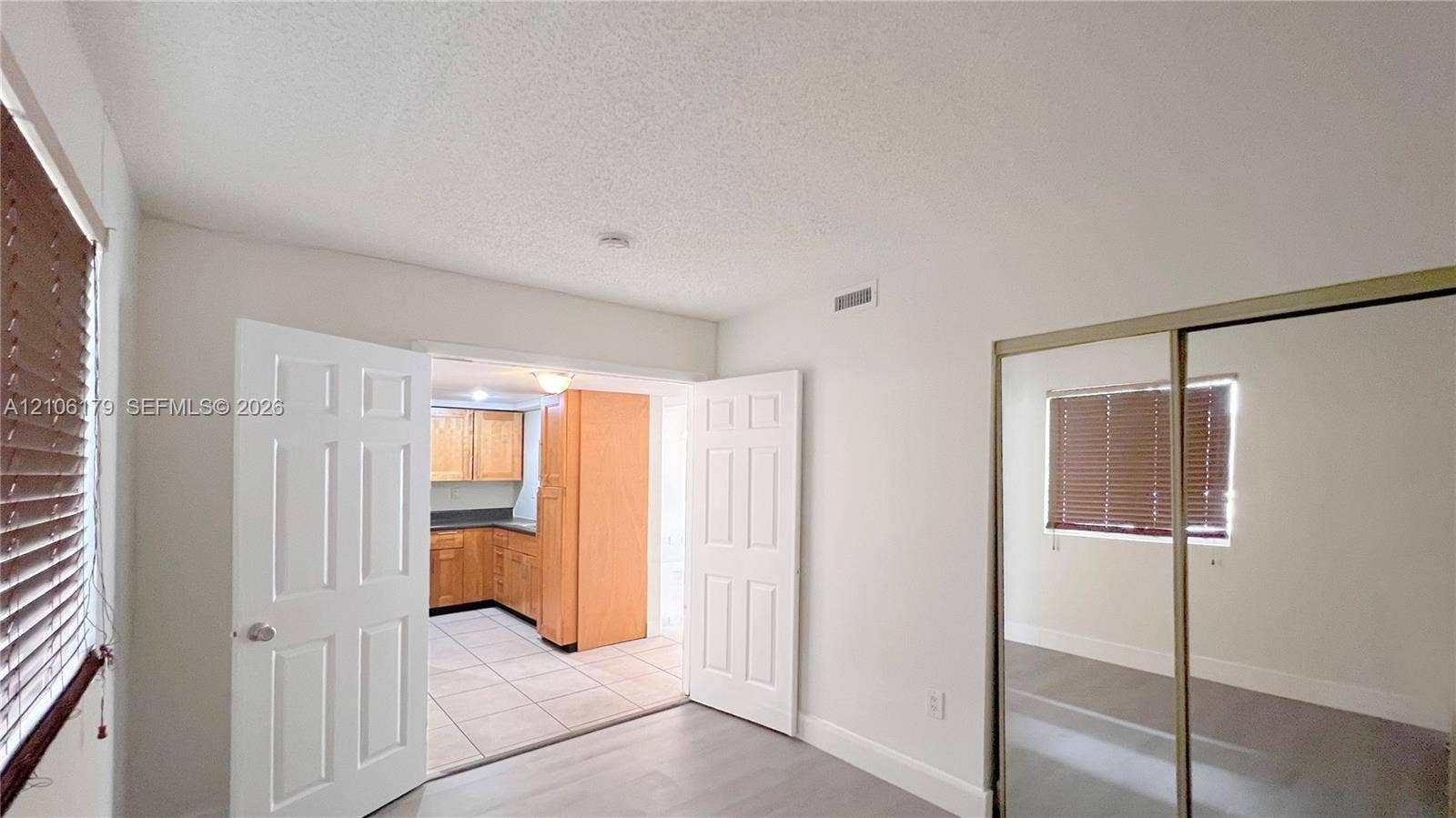 Interior space featuring light-toned flooring, wood-finish kitchen cabinetry, tile flooring in the kitchen, double-door entry, and sliding mirror-panel closet doors