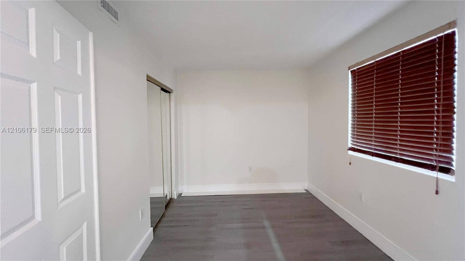 Room featuring neutral walls, wood-finish flooring, sliding mirrored closet doors, and a window with horizontal blinds