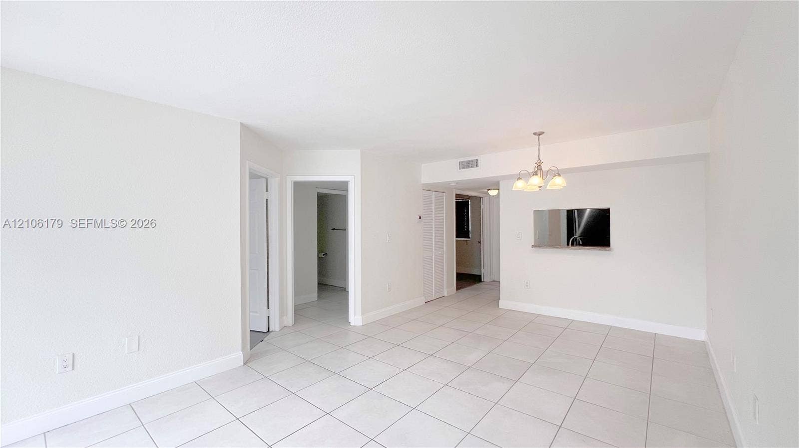 Neutral-toned interior featuring large-format tile flooring, a multi-bulb chandelier, a built-in wall niche, and crisp, light-colored walls