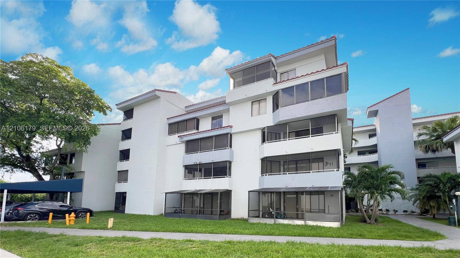 Multi-story residential building featuring stucco exterior, multi-level screened-in balconies, tile roof, and covered parking structure