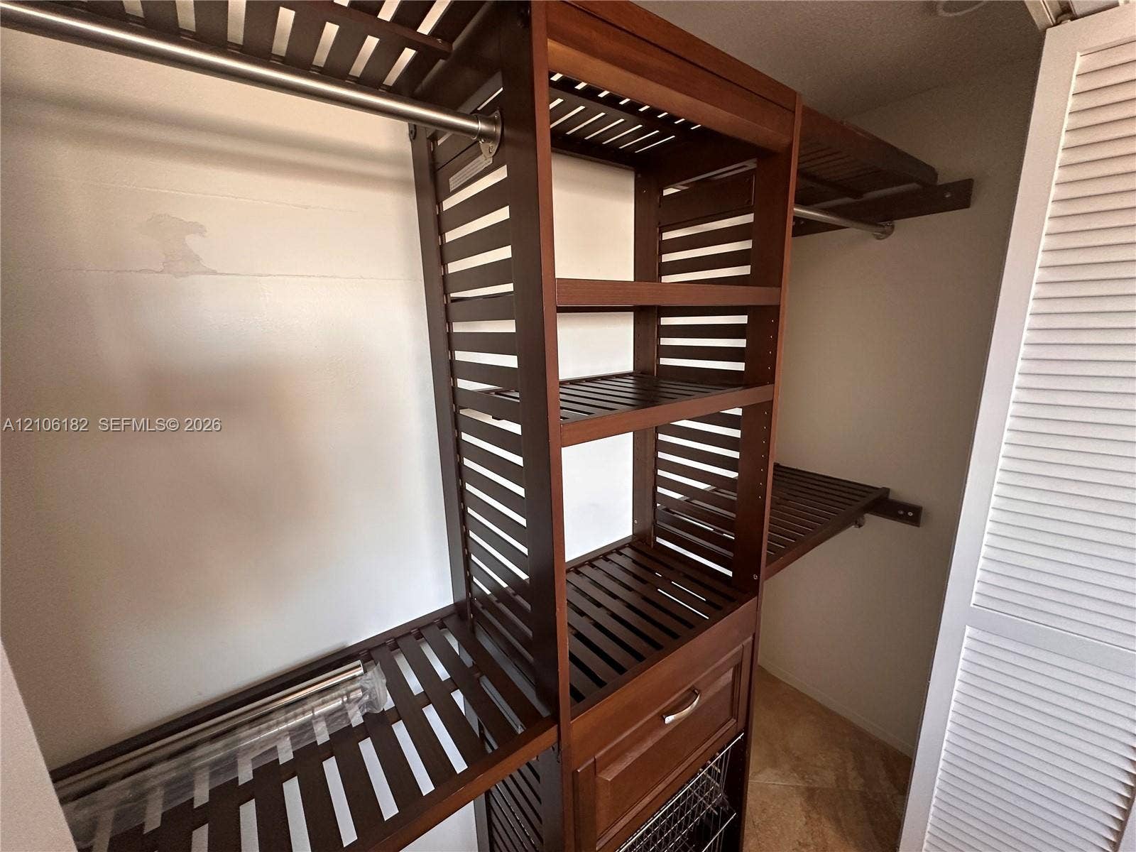 400 Golden Isles Drive, #40, Hallandale Beach, Hallandale Beach, FL 33009 Custom closet system featuring dark wood-finish open shelving, integrated hanging rods, a built-in drawer, and a lower pull-out wire basket, secured behind louvered doors