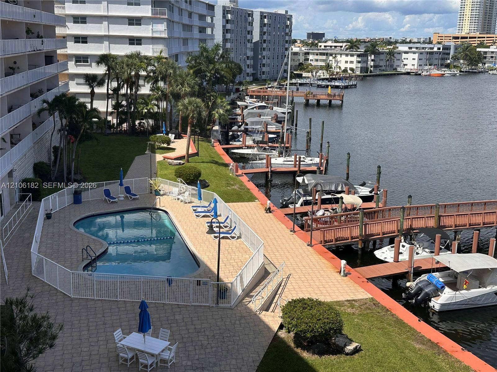 400 Golden Isles Drive, #40, Hallandale Beach, Hallandale Beach, FL 33009 Waterfront swimming pool area featuring paved decking, fenced enclosure, manicured lawn, and attached boat slips
