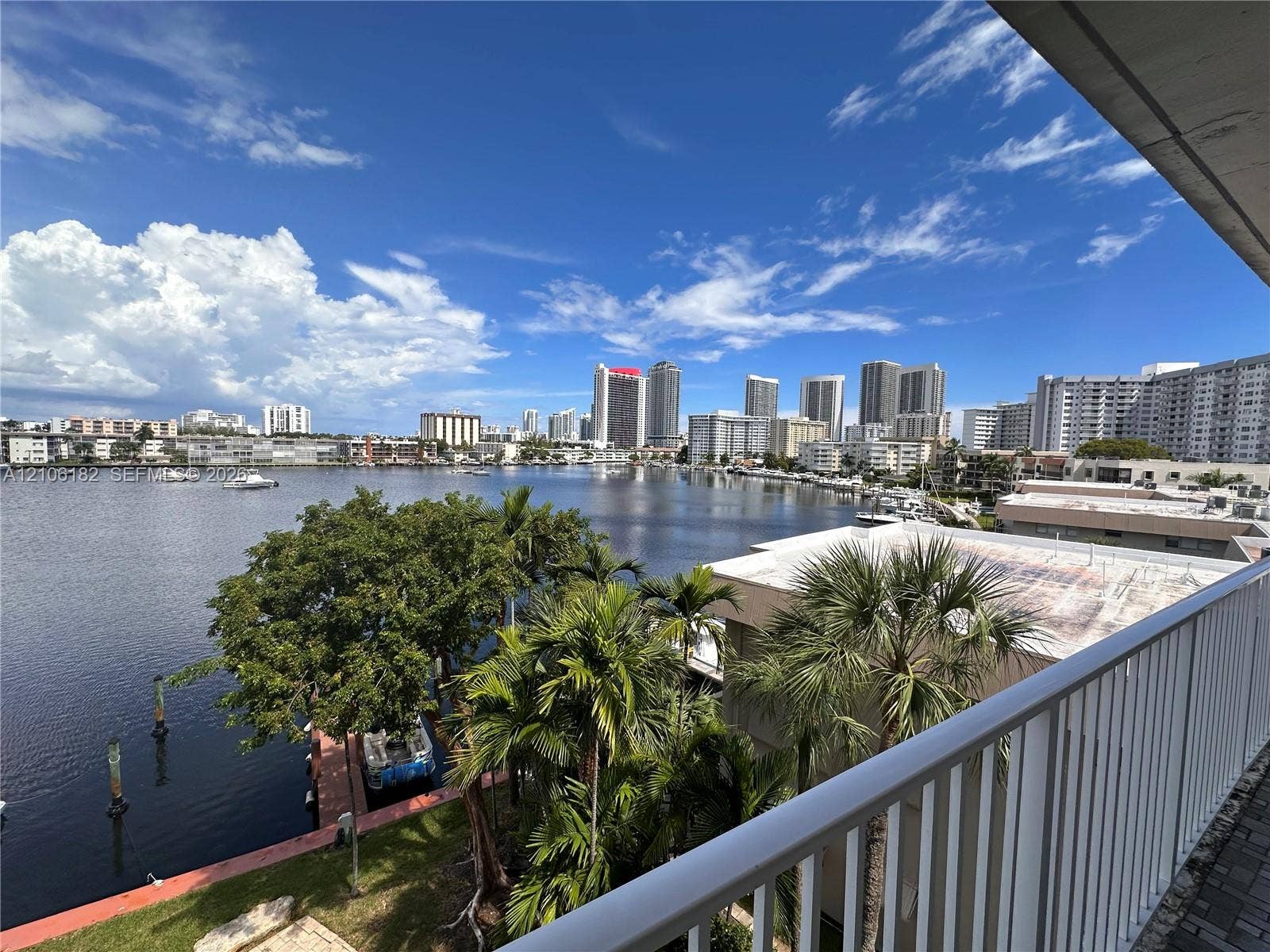 400 Golden Isles Drive, #40, Hallandale Beach, Hallandale Beach, FL 33009 Elevated balcony featuring a white metal railing, overlooking a waterway with mature palm trees and a skyline backdrop
