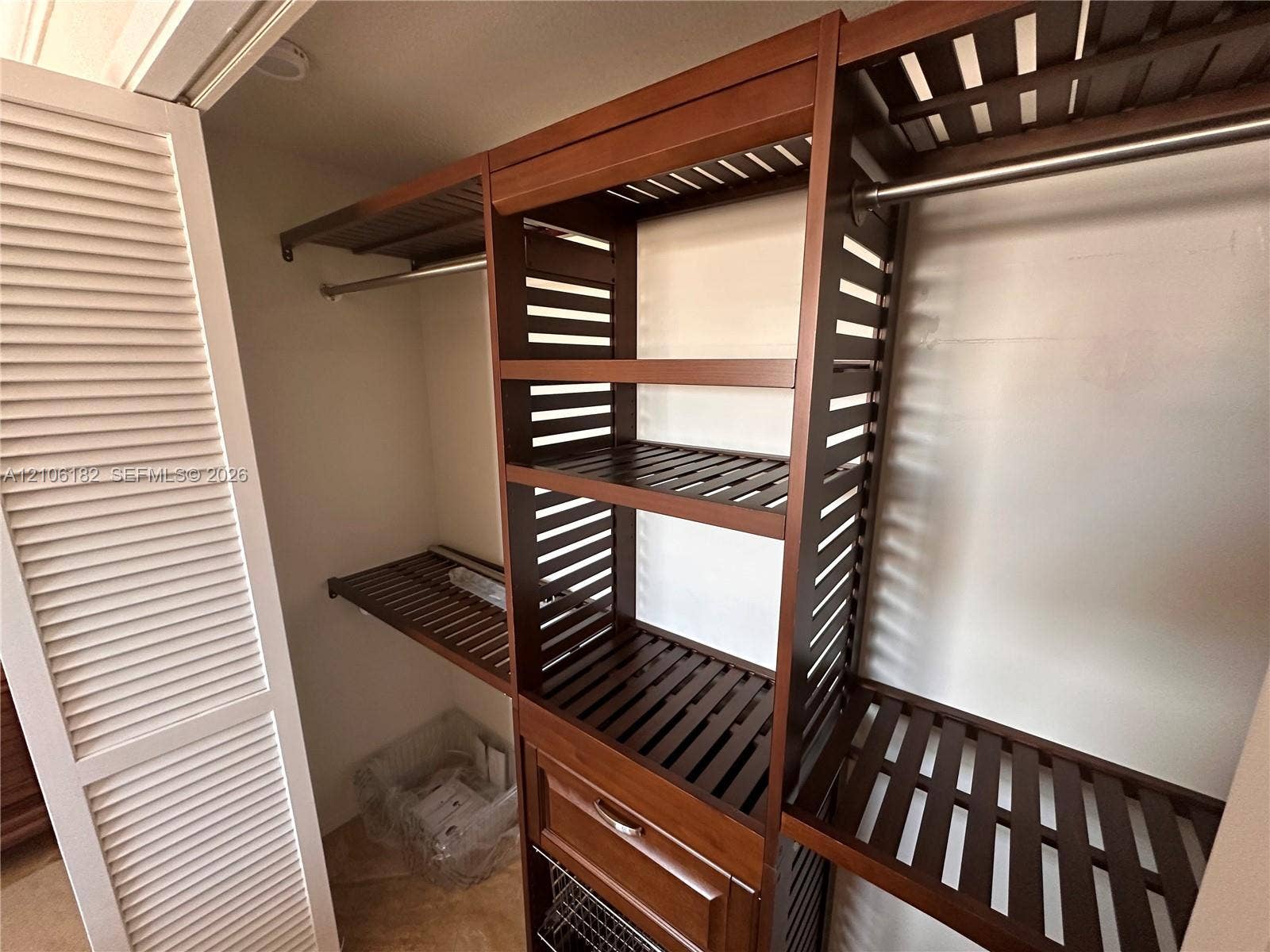 400 Golden Isles Drive, #40, Hallandale Beach, Hallandale Beach, FL 33009 Custom wood-finish closet organizer featuring slatted shelving, a built-in drawer, metallic hanging rods, and louvered folding doors