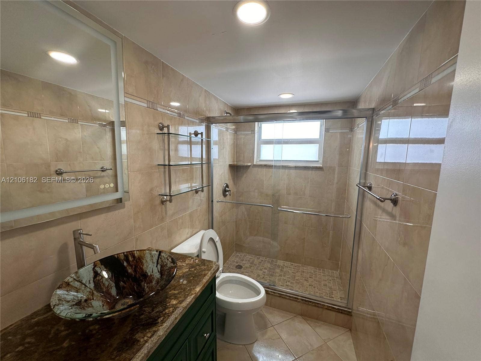 400 Golden Isles Drive, #40, Hallandale Beach, Hallandale Beach, FL 33009 Bathroom featuring tile wall surfaces, a vessel sink with a stone-finish countertop, a walk-in shower with a glass enclosure, and a wall-mounted light-up mirror