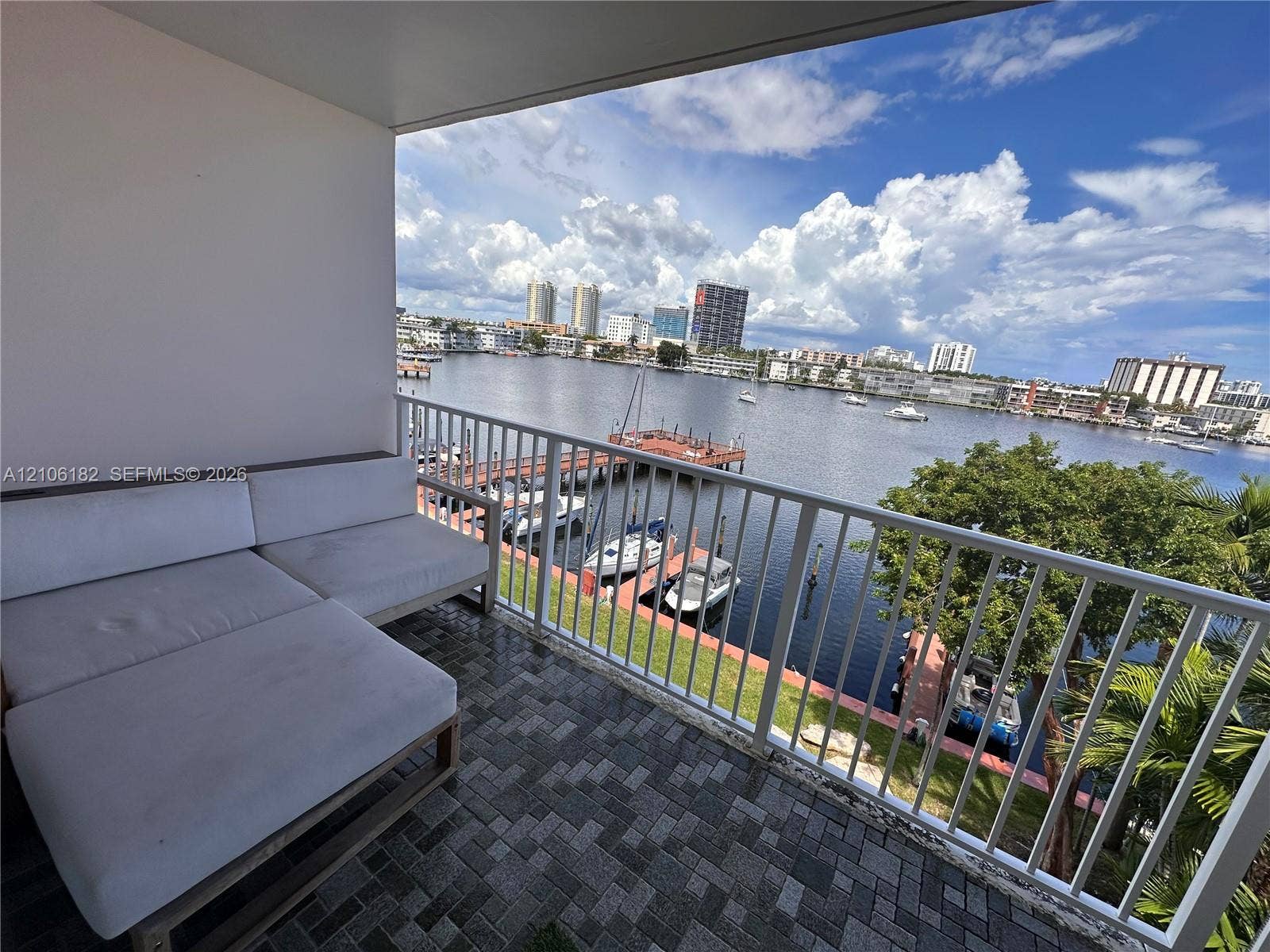 400 Golden Isles Drive, #40, Hallandale Beach, Hallandale Beach, FL 33009 Covered balcony featuring patterned stone paver flooring and a white metal safety railing overlooking a deep-water canal, boat slips, and a cityscape