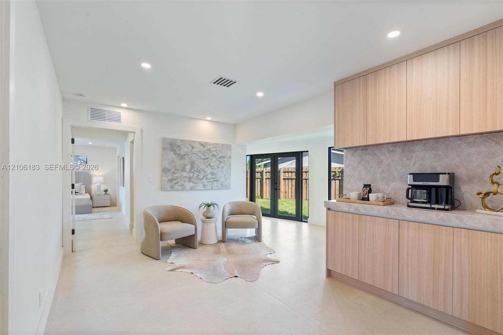 Light wood-finish cabinetry, neutral stone-finish countertops, recessed lighting, tile flooring, and black-frame glass exterior doors
