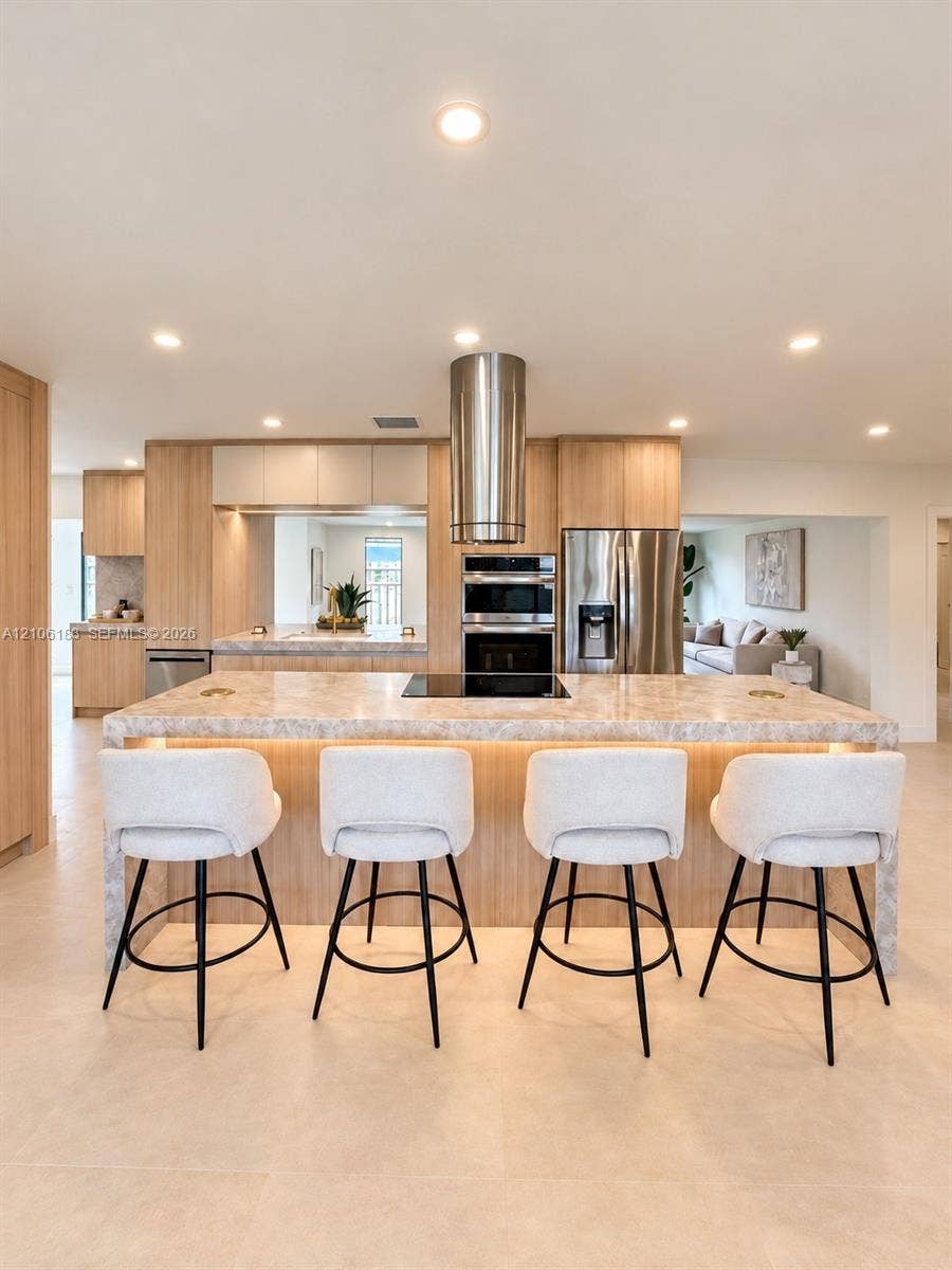 Kitchen featuring a central island with integrated cooktop, stone-finish countertops, stainless steel cylindrical range hood, custom wood-finish cabinetry, and recessed ceiling lighting