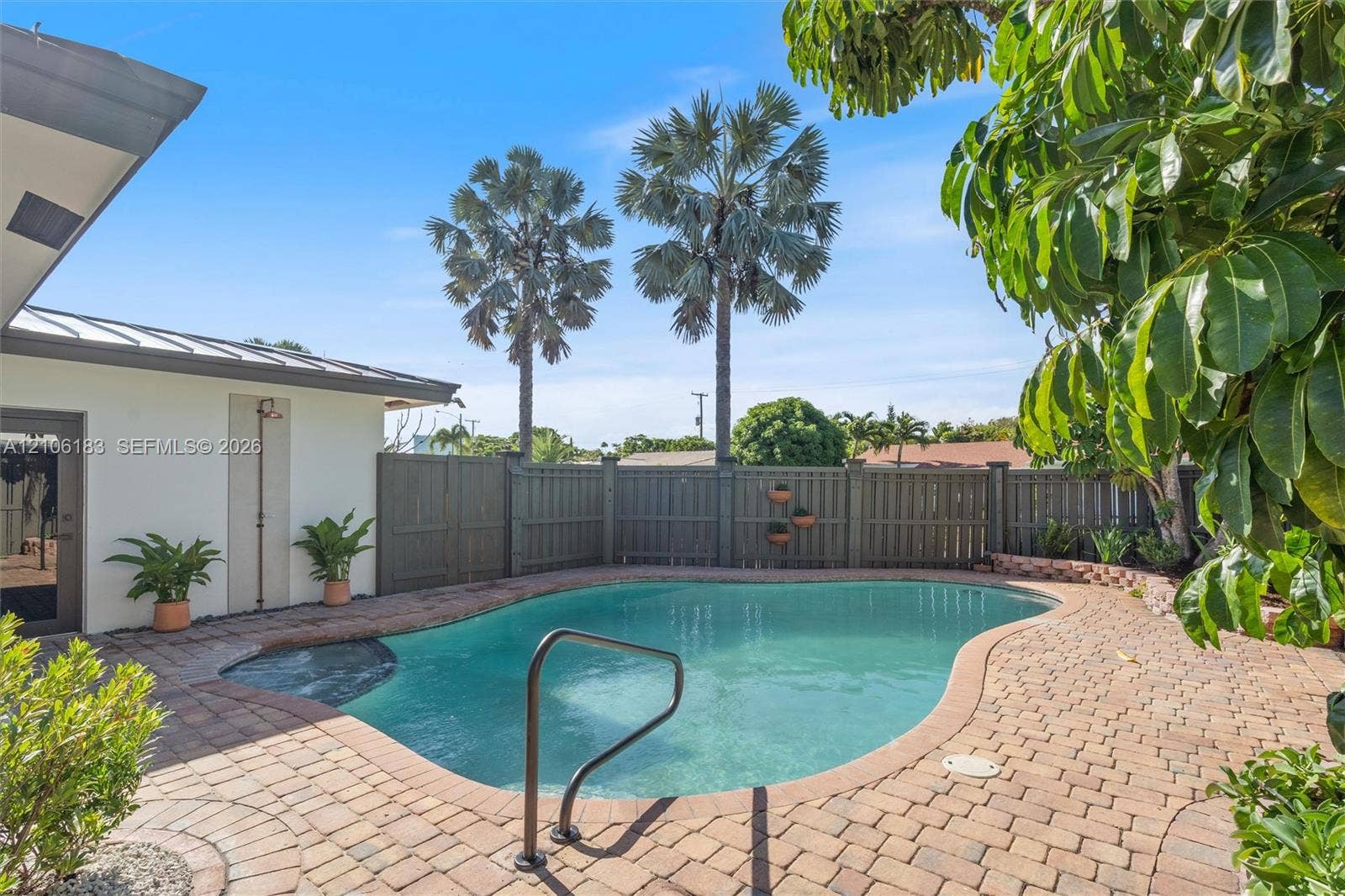 Freeform swimming pool with a metal grab rail, surrounded by a brick paver patio and enclosed by a wood privacy fence