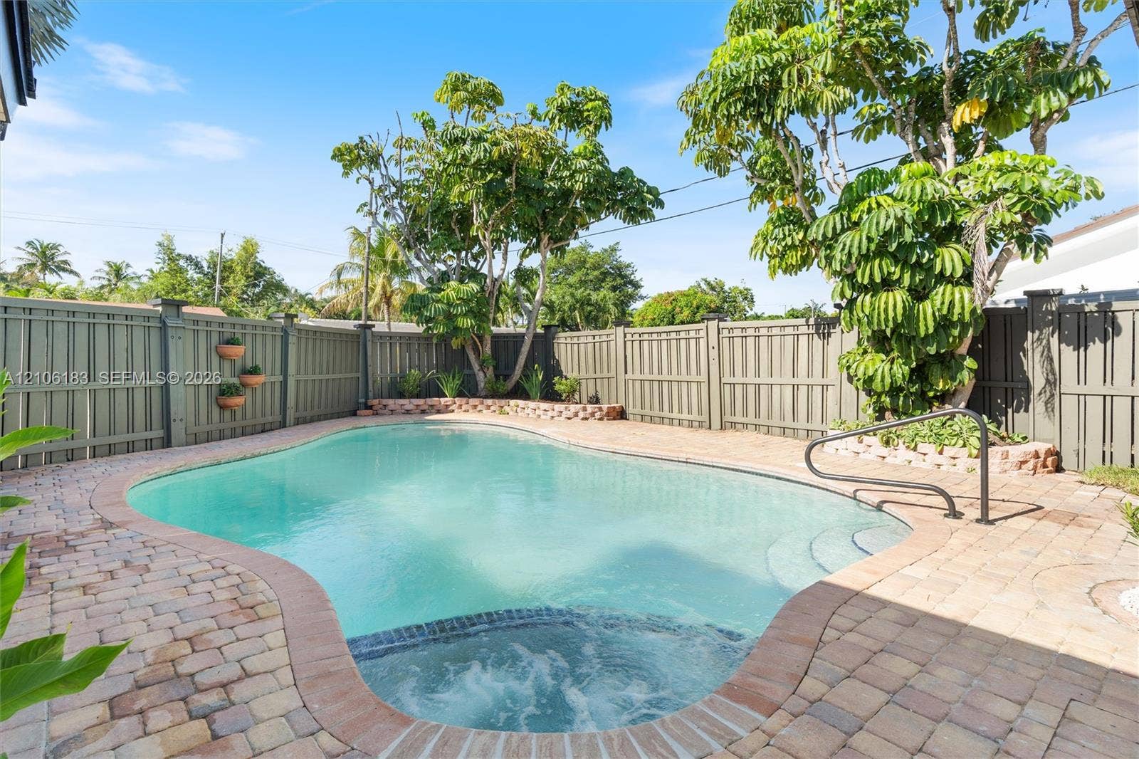 In-ground pool with integrated spa, bordered by paver decking and enclosed by perimeter fencing with mature landscaping