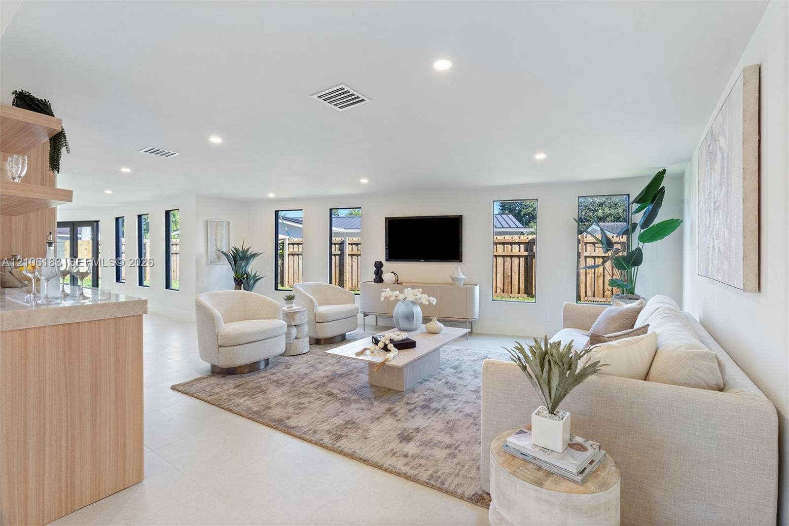 Open-concept interior featuring light-toned tile flooring, recessed ceiling lighting, vertical windows, and a built-in cabinetry unit