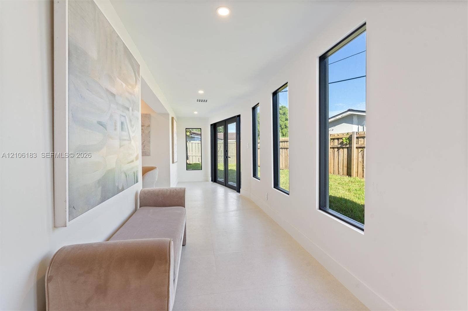 Neutral-toned tile flooring, recessed ceiling lighting, and multiple tall windows with dark frames