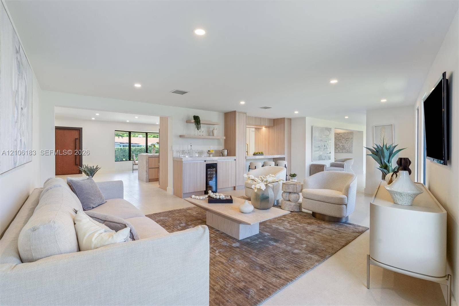Open-concept interior featuring light-toned neutral flooring, recessed lighting, and a built-in wet bar with a glass-front beverage refrigerator and open shelving